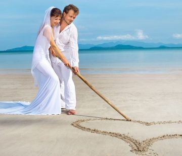 beautiful couple on the beach in wedding dress drawing heart
